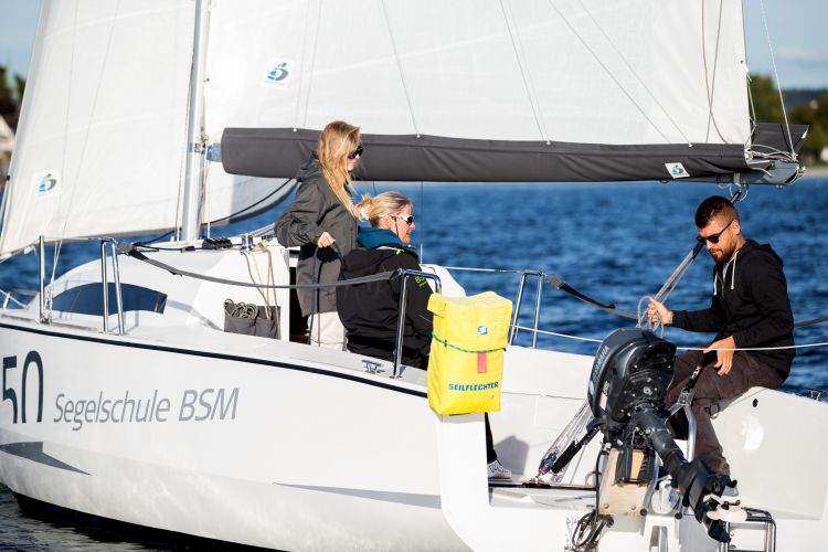 Drei Personen auf einem Segelschiff, wobei einer den Motor vom Wasser nimmt